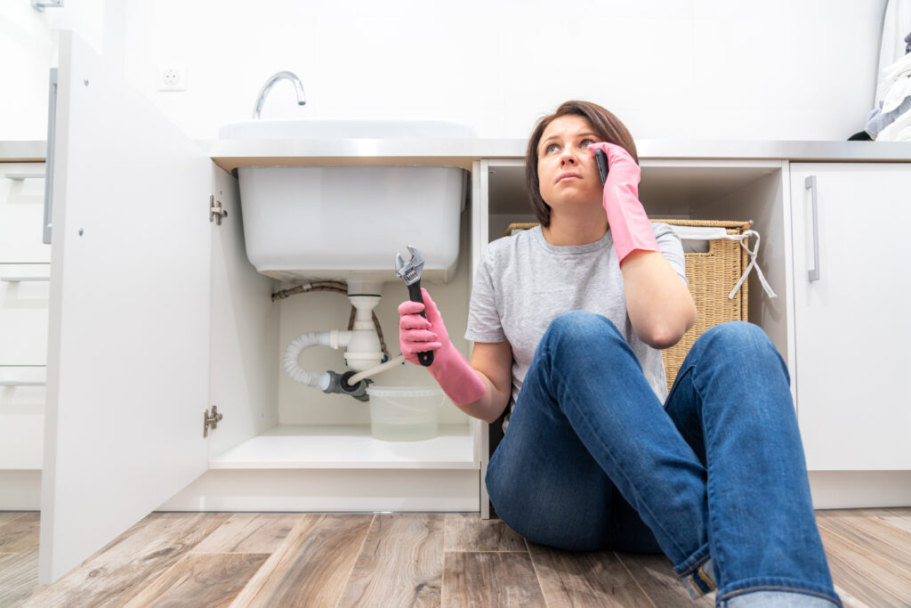 Woman sitting near leaking sink in laundry room calling for help